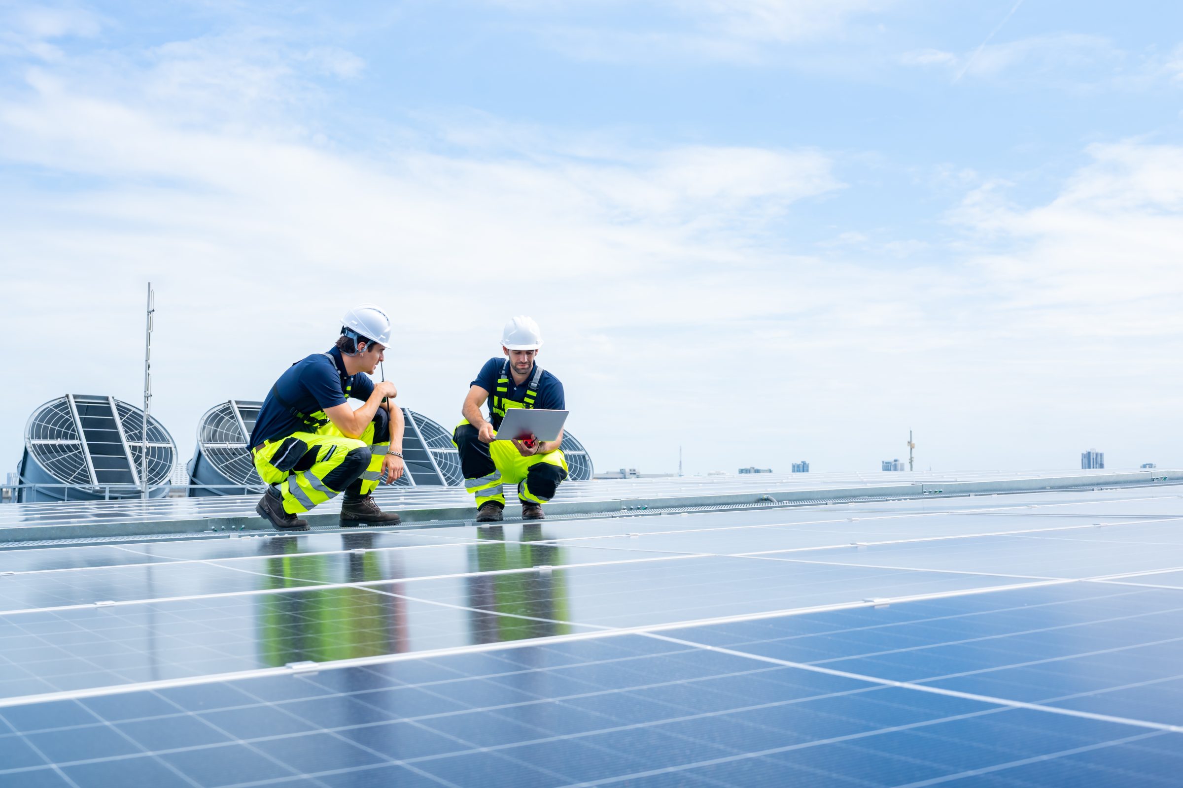 Two engineers kneeling on a rooftop solar installation reviewing a laptop