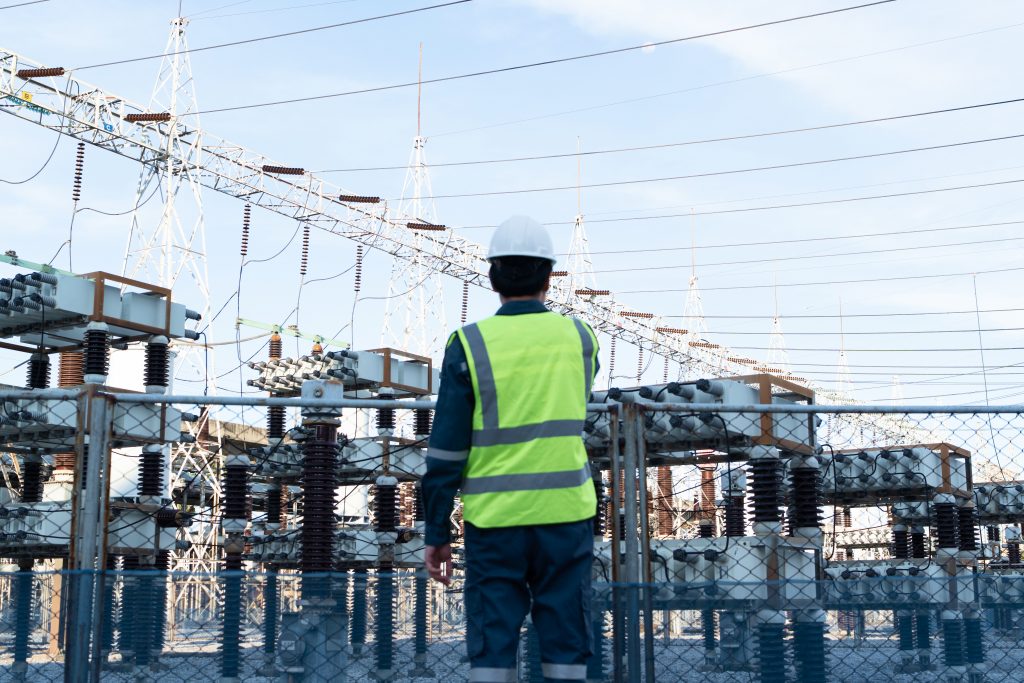 Field technician in a high-visibility vest surveying a substation