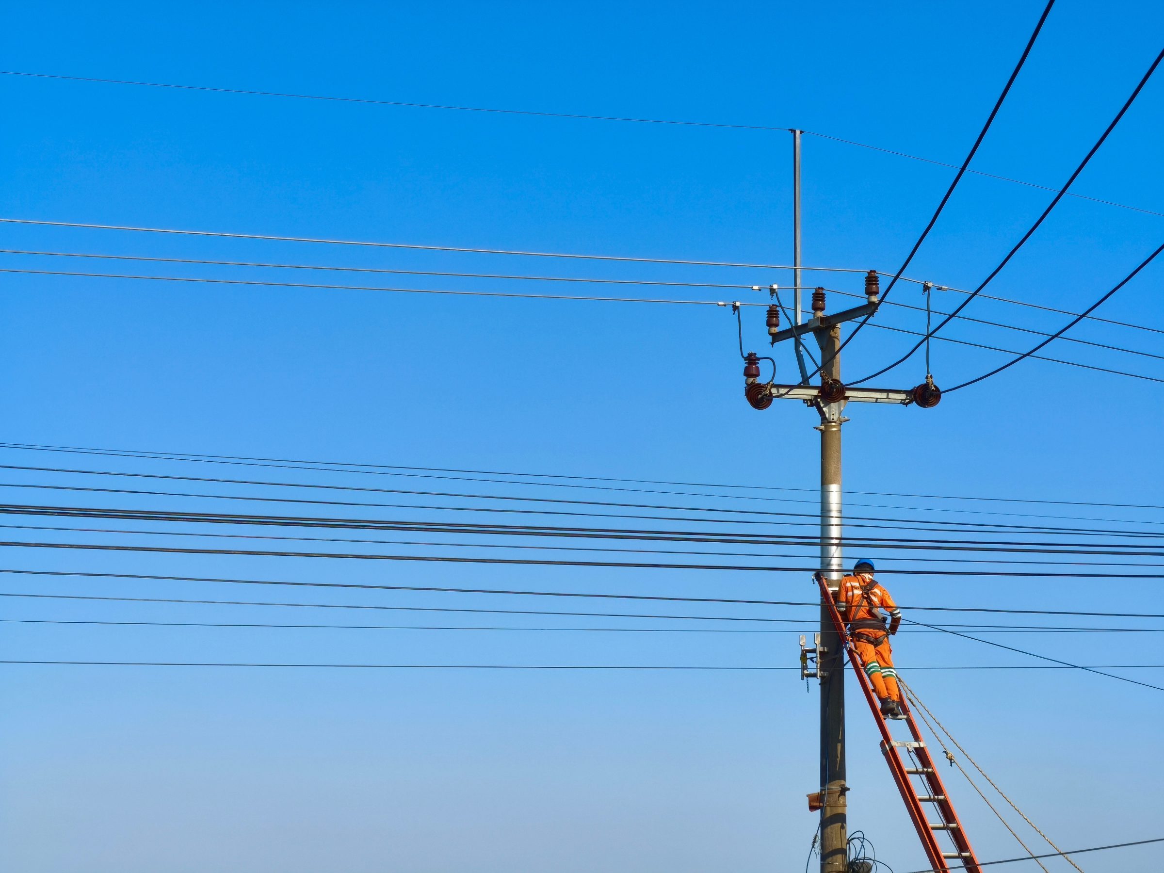 Lineworker on a ladder against a utility pole with overhead lines