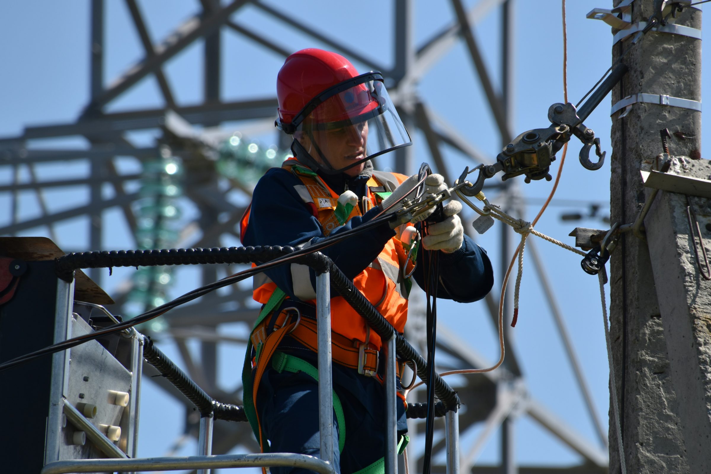 Lineworker in a red helmet and face shield working on energized equipment