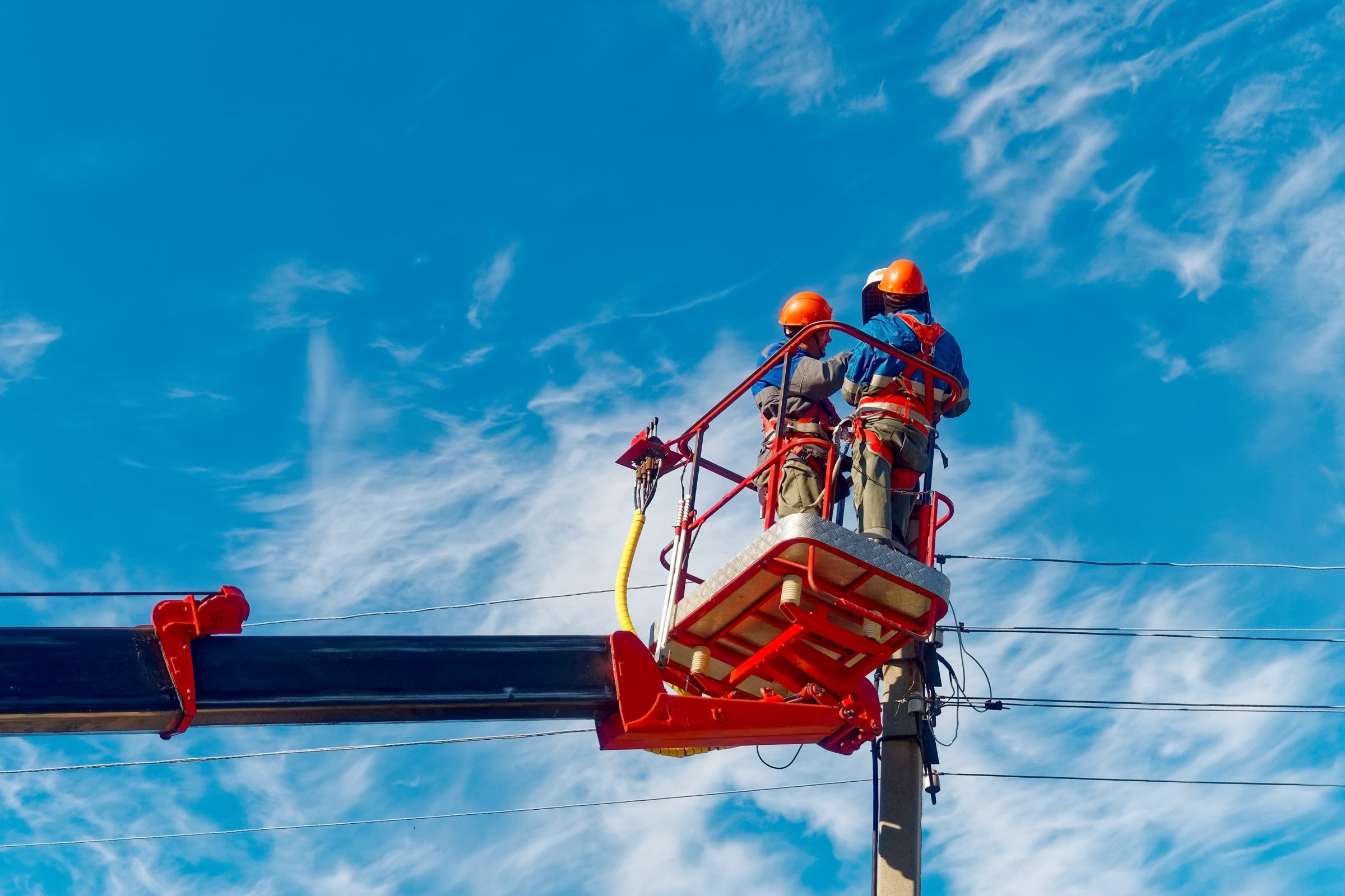 Two lineworkers in hard hats working from a bucket truck against a blue sky