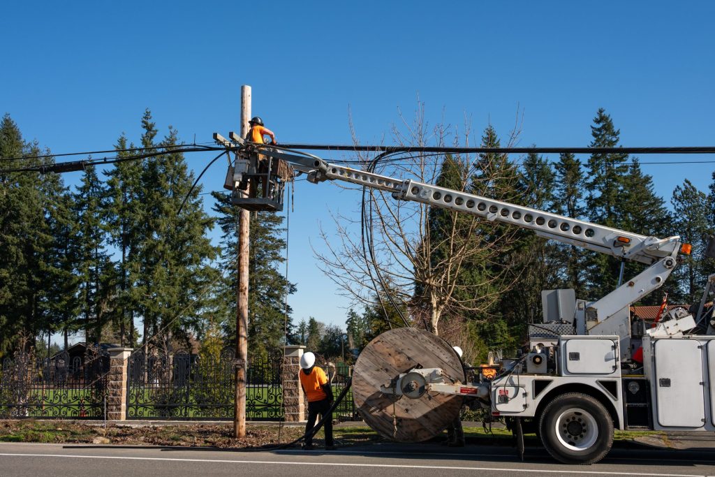 Crew pulling cable from a reel with a bucket truck beside a utility pole