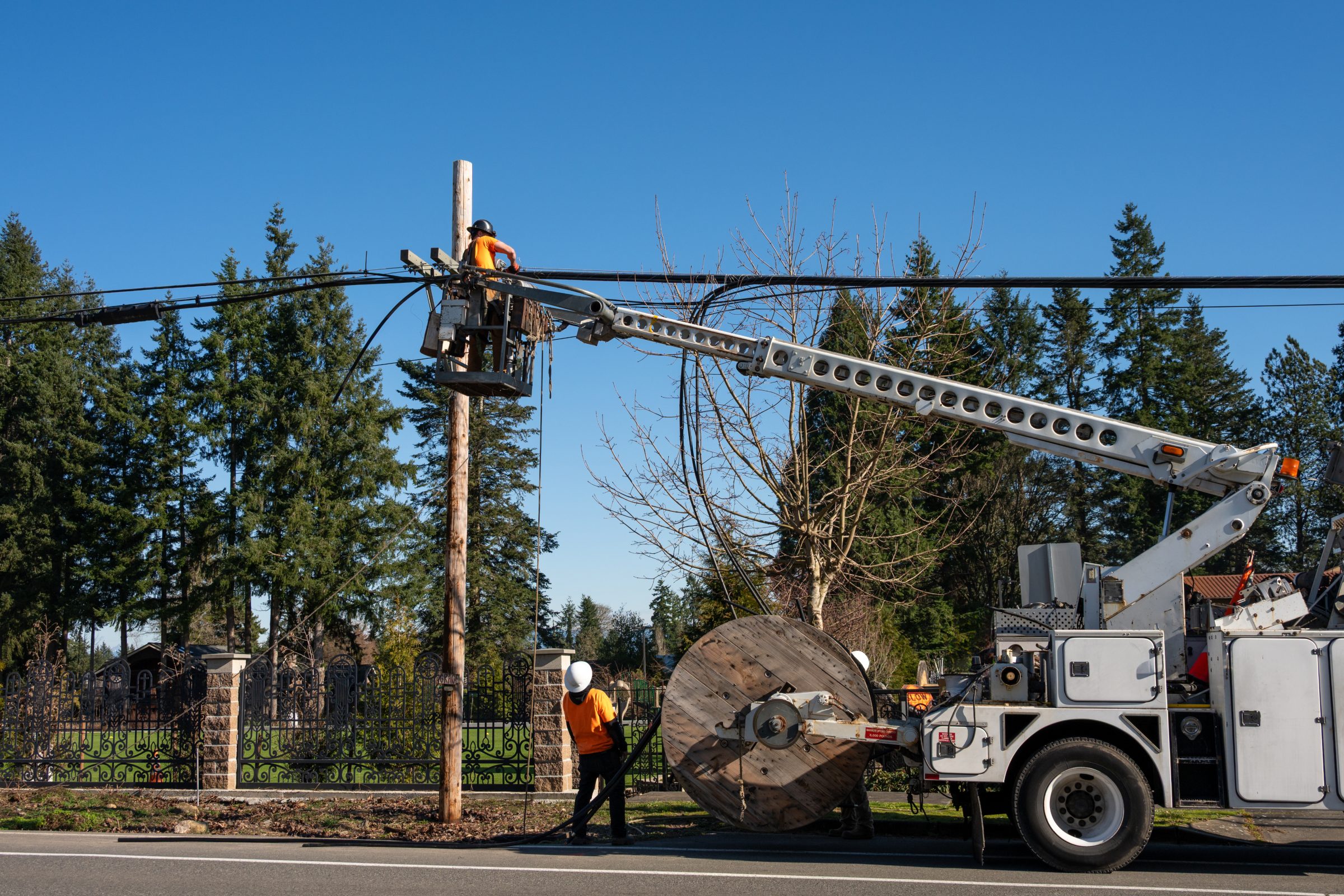 Crew pulling cable from a reel with a bucket truck beside a utility pole