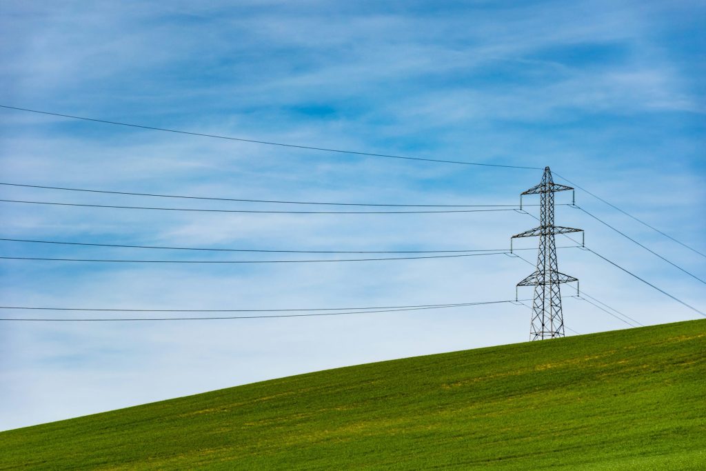 Transmission tower on a green hill under a blue sky